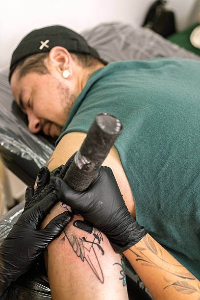 Tattoo artist wearing black gloves applying a new design on a client's arm in a professional studio setting