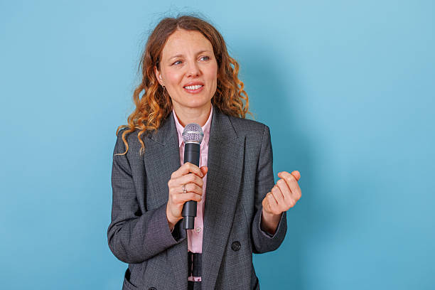istock Woman speaking on microphone delivering public presentation, communicating message to audience 2253539459