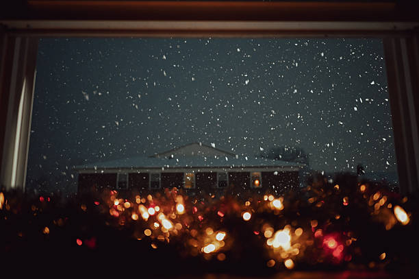 View from inside a warm home seeing snow falling on a dark winter night