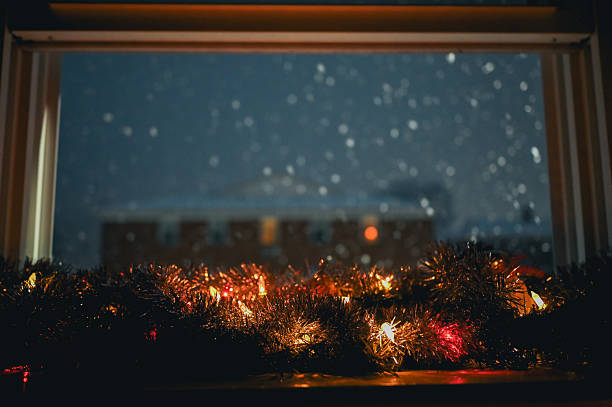 Christmas garland and lights decorating a window during a winter snowfall at night