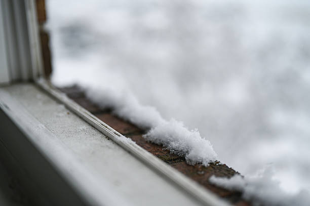 Snow accumulating on a brick windowsill during winter weather
