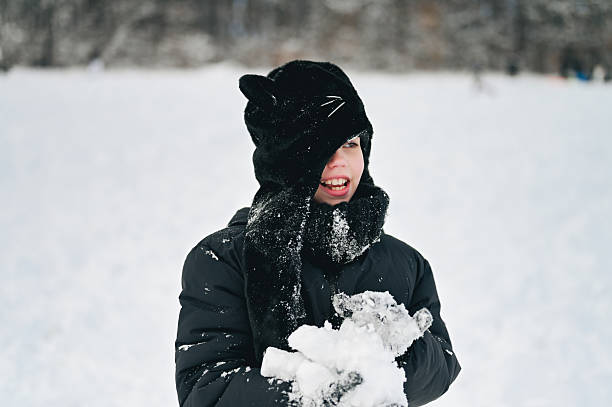 Child in black winter clothing holding snow and smiling outdoors