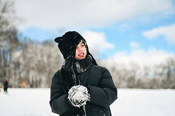 Child enjoying a snowy winter day, wearing warm clothing and making a snowball