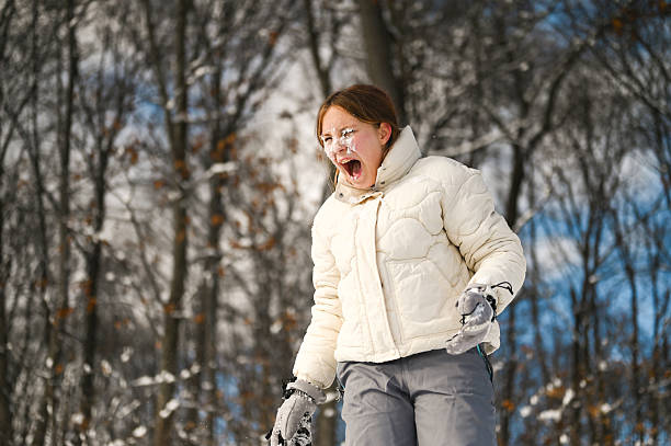 Teenager reacting to being hit by a snowball, screaming with her mouth wide open in winter