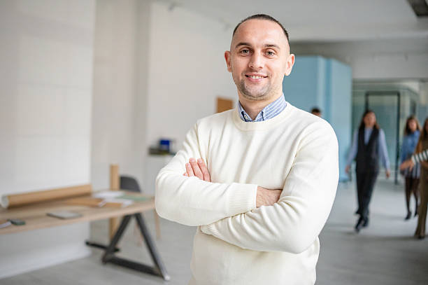 istock Man stands confidently in office setting while coworkers engage in work-related activities during the day 2253544143