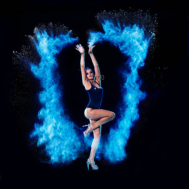Young woman jumping in blue powder cloud on black background
