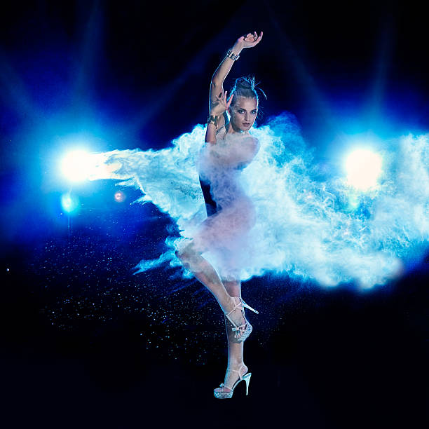 Young woman jumping in blue powder cloud on black background