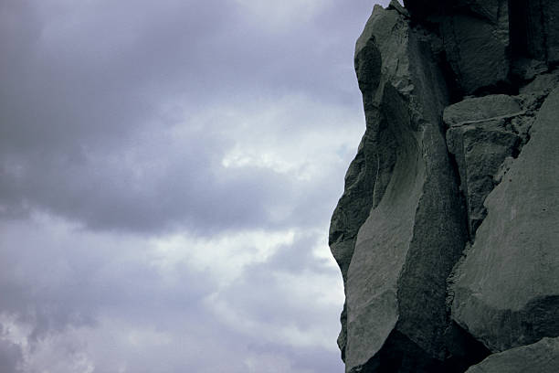 Lonely rock cliff against cloudy overcast sky background, creating an atmosphere of isolation and natural power in a moody landscape before the rain
