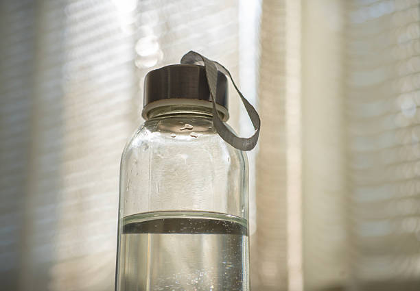 Glass water bottle containing clear unflavored water, standing in soft morning light, promoting healthy hydration and sustainable living