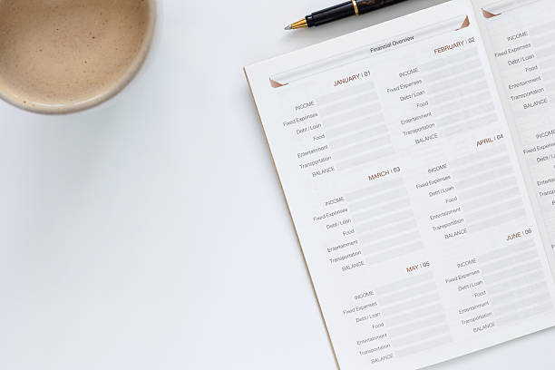 istock Financial planning concept with monthly budget planner notebook, pen, and coffee cup on white desk. Top view personal finance management and investment goals for saving money and wealth success. 2253553645