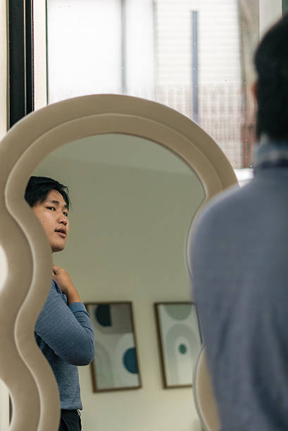 istock Young asian man looking at his reflection, preparing and grooming for the day 2253553772