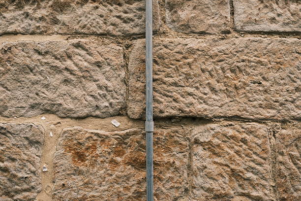 Close-up on a metal pipe on an old sandstone block wall.