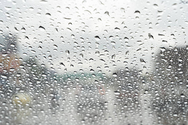 istock Raindrops on window glass with blurred city background, rainy day weather texture 2253557525