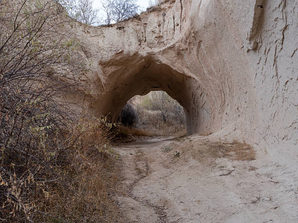 Eroded volcanic valley viewed from inside a rock-cut cave in Cappadocia, central Turkey. The cave opening naturally frames the landscape, combining geological formations with historic cave architecture typical of the region.