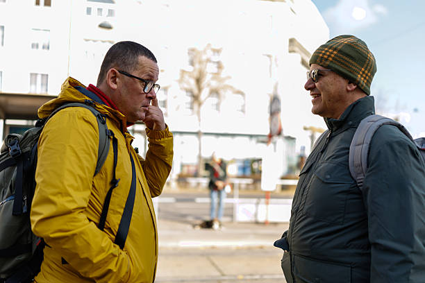 Two mature male friends standing on station and waiting for the tram in the city