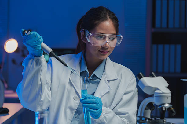 istock Young female scientist pouring blue liquid into test tube using pipette, conducting experiment in modern laboratory with microscope and advanced equipment 2253559041