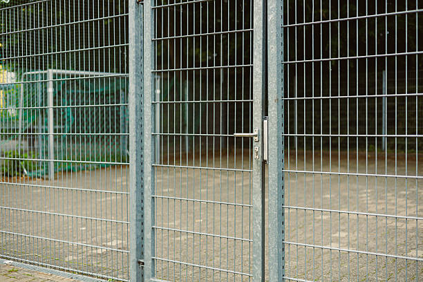 istock An Industrial Metal Fence Gate, situated in a bustling Urban Setting, serves as a Secure Barrier, featuring a dependable Lock Mechanism that ensures optimal safety and protection against intruders 2253562816