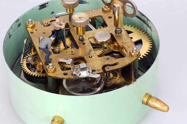 Two miniature figures navvy stand in old mechanical alarm clock among brass gears and stopping time.