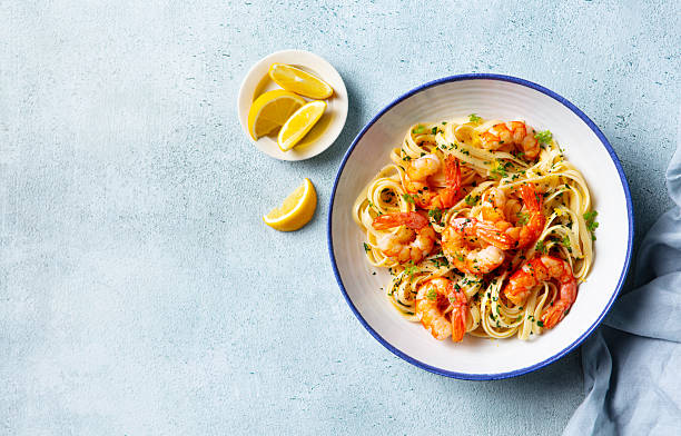 Shrimp pasta with lemon accents and fresh herbs. Light blue background. Copy space. Top view.