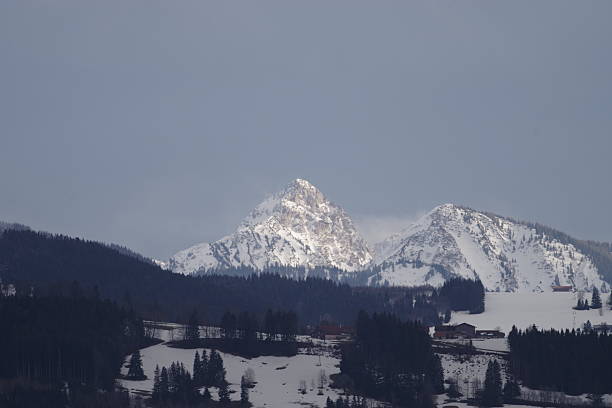 Beautiful mountain range covered in snow, with a cloudy sky in the background. The snow-covered peaks of the mountains are a stunning contrast to the dark blue sky. The scene is peaceful and serene