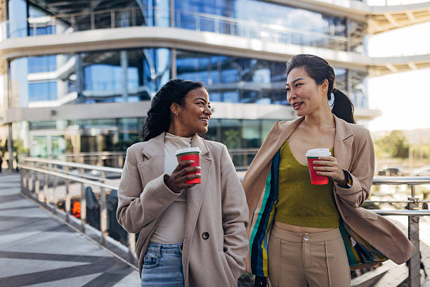 istock Two multicultural businesspeople walking in a modern office district, holding coffee cups and enjoying a break 2253574112