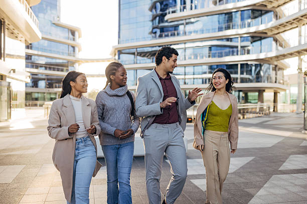 istock Multicultural group of colleagues walking together and talking outside a modern corporate building. Business lifestyle image highlighting diversity, teamwork, and a positive work environment 2253574323