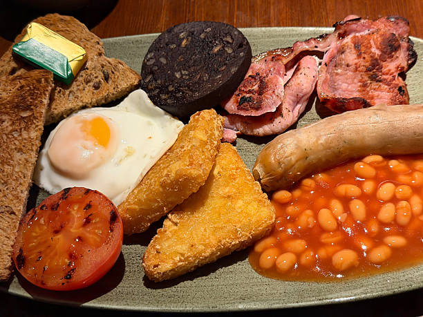 Image of full english fried breakfast with sausage, fried egg, bacon, black pudding, baked beans, hash brown, grilled tomato, traditional hearty morning meal