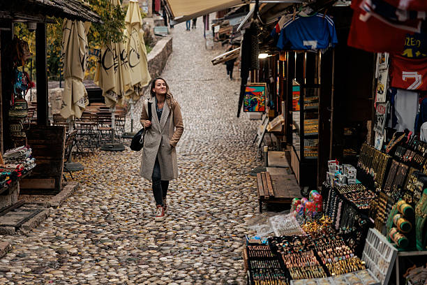 A woman explores a traditional market street, walking along a narrow cobblestone path surrounded by local shops and souvenir stalls. The scene reflects cultural discovery, authentic travel experience, and everyday life in a historic urban setting