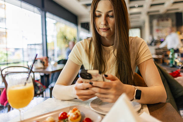 istock Attractive young woman is sitting and in a restaurant and using a mobile phone while having a breakfast 2253579251