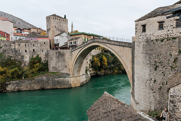 A historic stone bridge arches over a calm river, surrounded by traditional old town architecture and stone buildings. The scene represents travel, cultural heritage, architecture, and timeless European city landscapes.