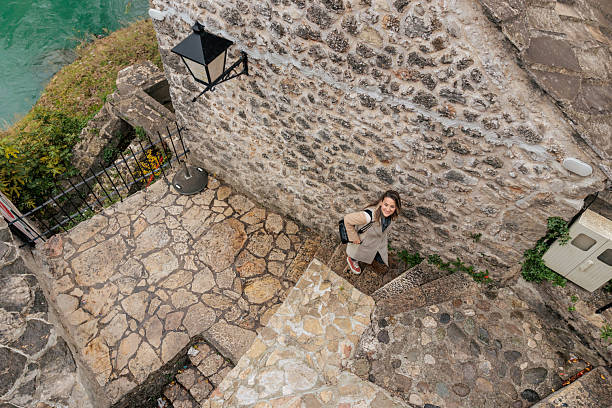 A woman walks along narrow stone steps in an old town, captured from an elevated angle as she looks upward.