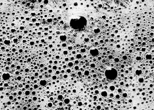 A high-contrast, black and white macro photograph of soap foam or shampoo suds, creating an abstract background texture. The image focuses on a dense pattern of bubbles varying in size, with some larger dark bubbles contrasting sharply against the white foam. The detail captures the organic, natural, and liquid texture of the detergent, suitable for use as a background, overlay, or abstract design element. This is a photograph, not an illustration or AI-generated image.
