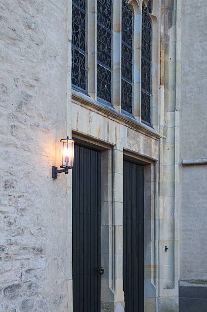 Stone church building with two dark doors, glowing lantern, and intricate gothic windows in borken, germany
