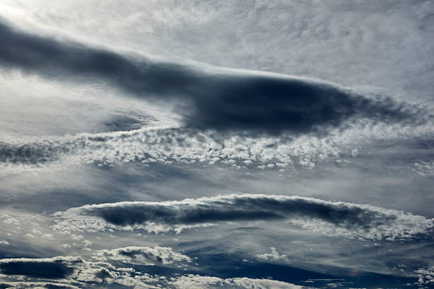 High-resolution cloudscape featuring tiered bands of cloudsfrom smooth, elongated dark layers to rippled, brighter texturesstretching across the frame. Subtle gradients of blue-gray and silver highlights create strong contrast and emphasize the wave structure associated with changing winds and unstable air. The panoramic composition provides generous copy space, making it ideal as a nature/Weather background for editorials, web headers, presentations, and ads touching on weather, climate, travel, uncertainty, or resilience. Horizontal, full frame; no people and no visible trademarks.