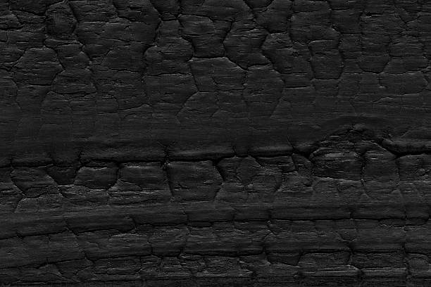 This Abstract Macrophotography Close-up, captured Directly Above in a High Angle View Flat Lay, fills the Full Frame with Burnt Hardwood Plank - Timber. The Black Color Wood Grain, Cracked Pattern, and Char-Grilled Tied Knot form Weathered Old Wood - Material, showing the Aging Process of Being Fireda Fire - Natural Phenomenon that turned a Tree into Coal Firewood. Grunge Image Technique, retro style Vignette, and Textured Effect yield Minimalist Art Backgrounds, Wallpaper - Decor, and Template versatility. The Blank, Empty, Dark Surface Level scene offers Copy Space for Design, Rustic Table Top View mock-ups, or Building Exterior panel graphics on Built Structure projects. Peeling Off Plant Bark, Rough stains, Dirty, Rusty, Broken edges depict Destruction and Crisis. Vibrant Color sparks enliven the material's Pattern, while No people remain in sight.