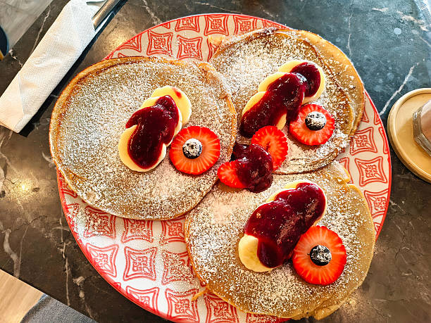 Three pancakes with bananas, strawberry jam and pieces of strawberries on a plate.