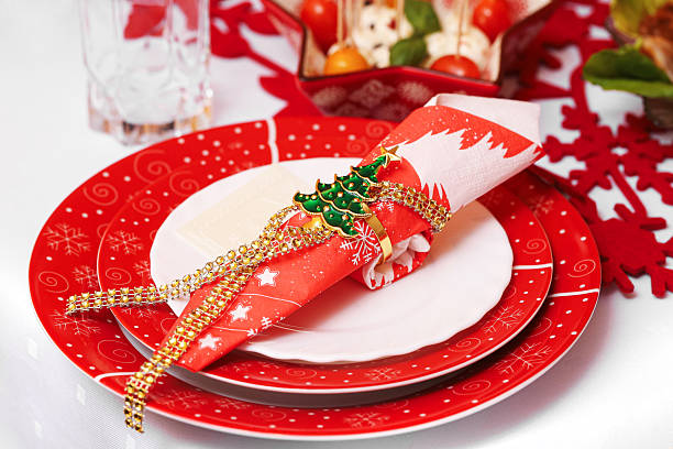 Silver and white Christmas place setting using a white plate trimmed with silver and silver tableware, a silver and green decoration is on top of white napkin. Horizontal image.