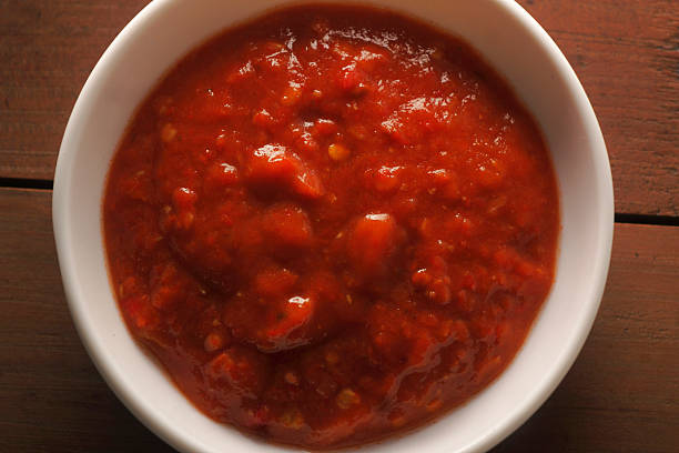 Spicy red chutney served in a white bowl, made with red chilies and traditional Indian spices, shot on rustic wooden background for food photography.