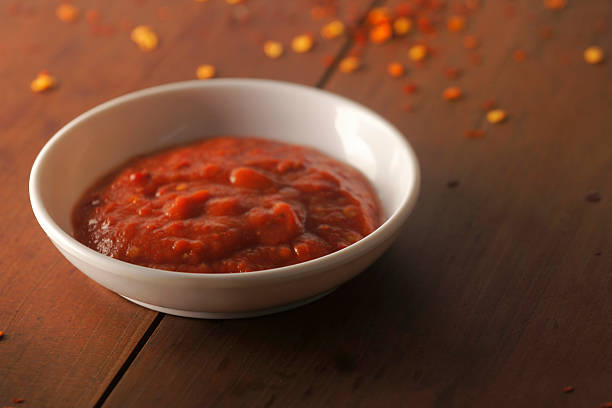 Spicy red chutney served in a white bowl, made with red chilies and traditional Indian spices, shot on rustic wooden background for food photography.