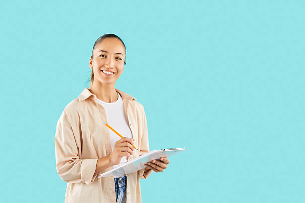 istock Happy Asian college student girl writing notes on clipboard on blue copy space background 2253609395