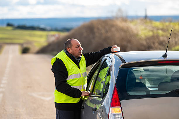 Driver placing a V16 warning or emergency beacon with a broken-down vehicle on the road, calling for a tow truck, using the emergency signal and warning triangle. This beacon will be mandatory in Spain by 2026. Tordesillas, Valladolid, Castile and León, Spain, Europe - December 21, 2025.