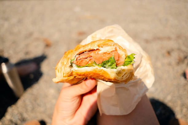 Close-up shot of a fresh croissant with smoked salmon and green lettuce partially eaten, perfect for healthy snack and outdoor food concepts.