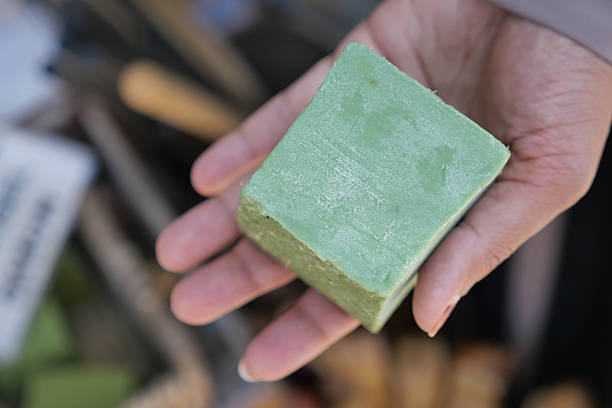 A person holds a fresh green bar of handmade soap at a bustling market.