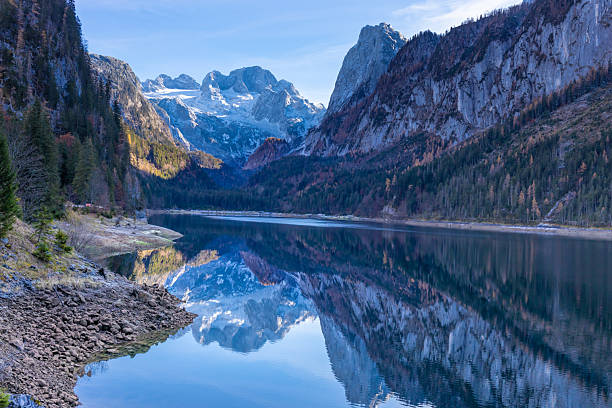 Gosausee lake in Austria with clear alpine water reflecting Dachstein mountains and surrounding forest. Natural mountain landscape showing glacial lake, rocky peaks, outdoor environment, tourism destination, European Alps scenery, nature background, and freshwater ecosystem