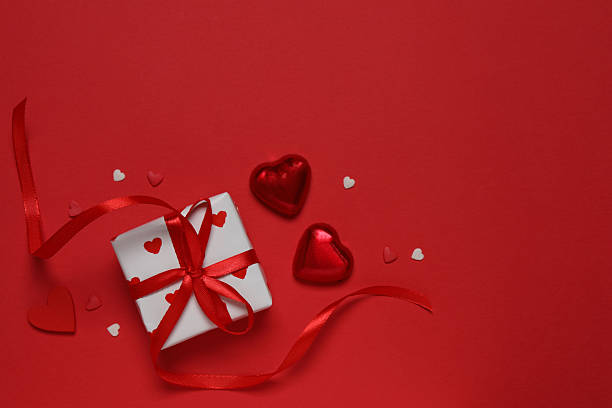 istock Festive gift box with red hearts on color background 2253614488