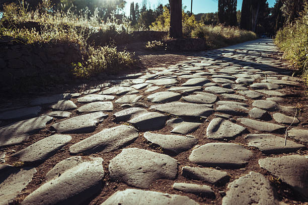 Close-up view of the original stone paving of the Appian Way, showing irregular basalt cobblestones worn smooth by centuries of use. Low-angle sunlight emphasizes texture, shadows, and the enduring construction of one of the oldest Roman roads, symbolizing ancient engineering and historical continuity.
