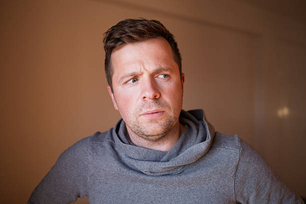 A close-up portrait of a bdy conscious man sitting in his bathroom. He looks concerned and has some health concerns playing on his mind.\n\nVideos available for this scenario.