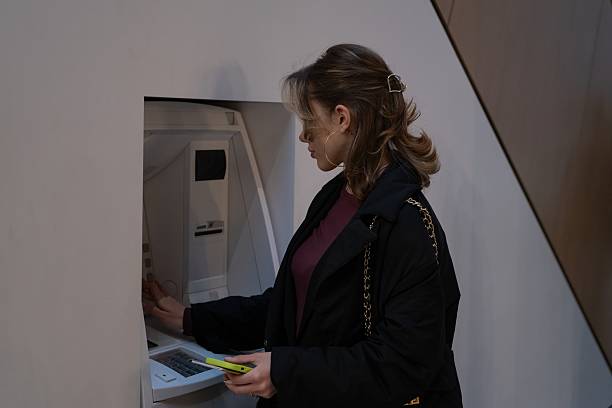 istock Woman entering PIN at ATM while holding smartphone 2253630853
