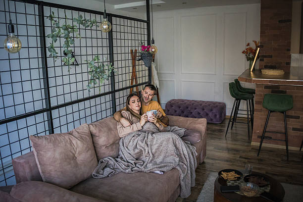 istock Romantic, loving couple sitting embraced on the sofa covered with blanket in cozy home sharing tender moments of love while drinking tea or coffee from the cups. 2253631721