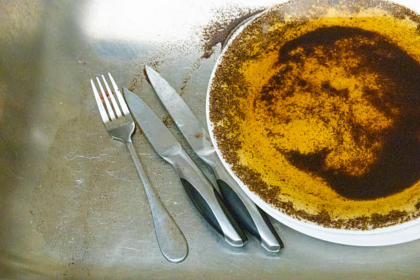 Used plate with curry residue and metal cutlery on a stainless steel surface, showing food leftovers and messy kitchen atmosphere.
